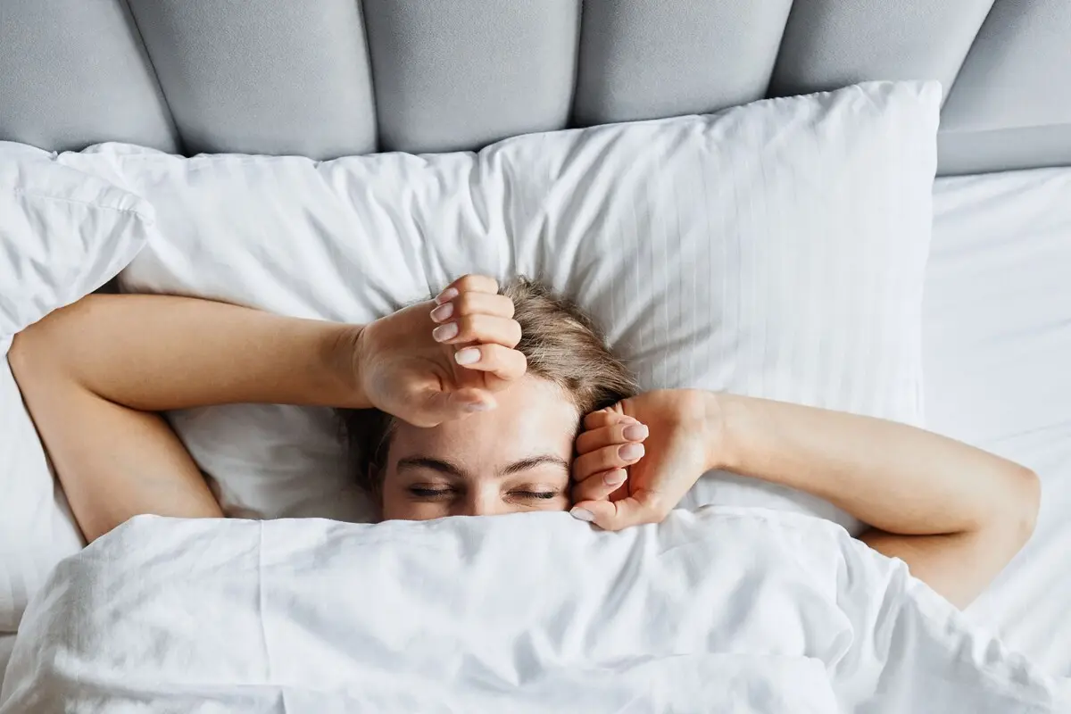 A woman waking up rested in a bright white bed — good sleep supports IVF preparation