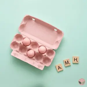 Pink egg carton with three eggs left and Scrabble tiles spelling AMH